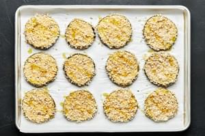 12 Eggplant slices dredged in flour, egg and panko arranged on a parchment lined baking sheet.