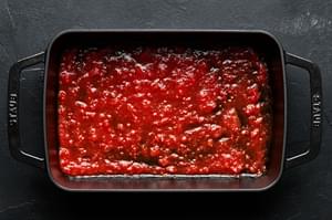 Marinara spread out in the bottom of a baking dish