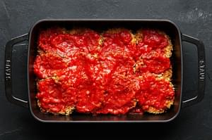 Breaded eggplant sliced topped with marinara sauce in a large baking dish.