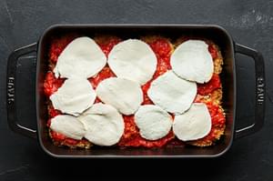 Breaded eggplant slices topped with marinara sauce and fresh mozzarella cheese slices in a black casserole dish.