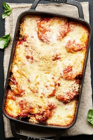baked Eggplant parmesan in a black cast iron 9x13 casserole dish surrounded by fresh basil.