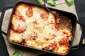Eggplant parmesan in a black baking dish with a metal serving spoon.