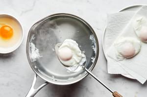 eggs being poached in a pot and scooped out with a slotted spoon