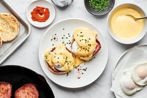 homemade eggs Benedict made with Canadian bacon and homemade hollandaise sauce on a plate surrounded by the ingredients