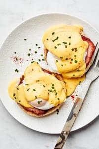 homemade eggs Benedict made with Canadian bacon and homemade hollandaise sauce on a plate with a fork