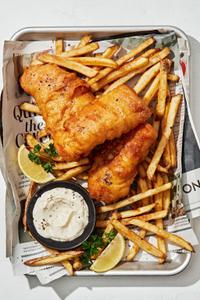 homemade fish and chips on a parchment covered rimmed baking sheet served with tartar sauce and lemon wedges
