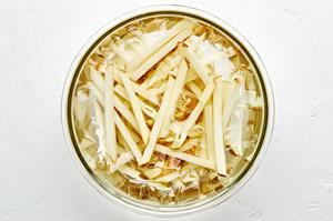 raw potatoes cut into French fries soaking in a bowl of ice water