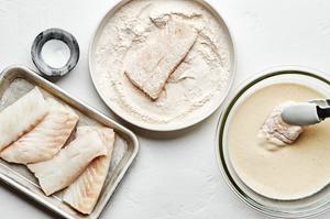 raw cod being dipped into homemade beer batter and then into a flour and seasoning mixture ready to be fried for fish & chips