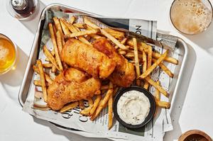 homemade cod fish and chips on a parchment covered rimmed baking sheet served with tartar sauce and lemon wedges