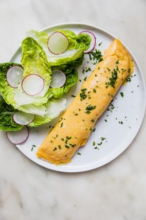 a homemade French omelette sprinkled with parsley on a plate next to a simple salad of crisp lettuce and thinly sliced radish