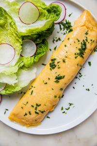 a homemade French omelette sprinkled with parsley on a plate next to a simple salad of crisp lettuce and thinly sliced radish