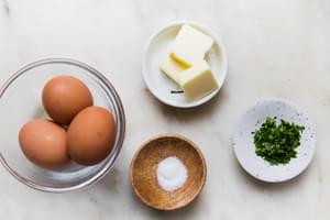 3 eggs, butter, salt and chopped fresh parsley in bowls on the counter to make a homemade French omelette