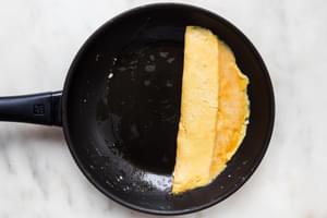 a homemade French omelette being rolled in a non stick frying pan with pan with melted butter