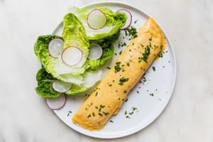 a homemade French omelette sprinkled with parsley on a plate next to a simple salad of crisp lettuce and thinly sliced radish