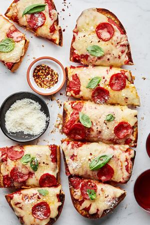 homemade french bread pizza cut into slices next to bowls of parmesan and red pepper flakes for topping
