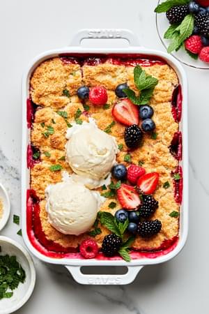 fresh berry cobbler in a 9x13 baking dish topped with 2 scoops of vanilla ice cream, additional fresh berries and fresh mint