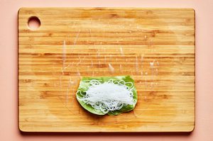 rice paper topped with lettuce and vermicelli rice noodles on a wooden cutting board to make fresh spring rolls