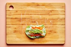 rice paper topped with lettuce, vermicelli rice noodles and julienned vegetables on a wooden cutting board