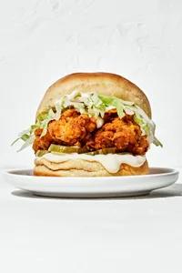 a homemade fried chicken sandwich on a brioche bun with garlic aioli, sliced pickles and shredded iceberg lettuce