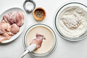 raw chicken thighs, an egg mixture, a flour dredging mixture and salt and pepper in bowls to make fried chicken