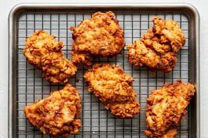 homemade fried chicken cooling on a wire rack on top of a baking sheet