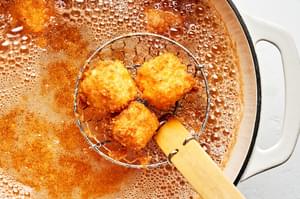Fried cheese breaded with flour, spices, eggs and panko being scooped out of a pot of vegetable with a spider strainer