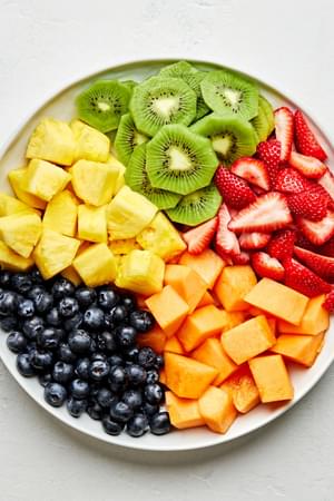 chopped Cantaloupe, Pineapple , Strawberries, Blueberries and Kiwis in sections on a platter for making fruit salad
