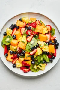 homemade fruit salad mixed with an orange juice dressing and mint leaves on a platter on the counter