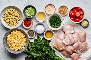 chicken thighs, corn, lima beans, basil, cilantro, tomatoes, green onions olive oil and spices in bowls on the counter