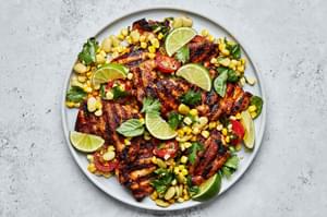 homemade Grilled chicken Thighs with Succotash on a serving platter topped with lime wedges for garnish
