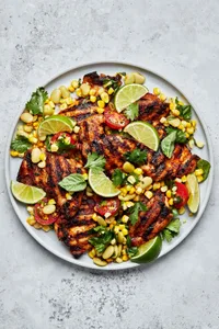 Grilled chicken Thighs with Succotash on a serving platter topped with lime wedges for garnish