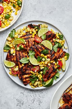 homemade Grilled chicken Thighs with Succotash on a serving platter topped with lime wedges for garnish