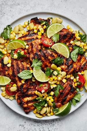 homemade Grilled chicken Thighs with Succotash on a serving platter topped with lime wedges for garnish