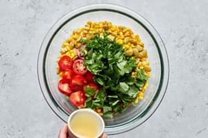 lime juice being poured over tomatoes, cilantro, basil and sautéed lima beans, corn and green onion to make succotash