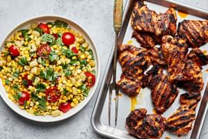 grilled chicken thighs on a baking sheet next to a bowl of homemade succotash made with corn and lima beans