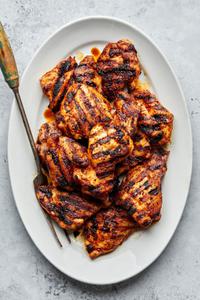 Grilled chicken thighs with beautiful grilled marks on a platter with a serving fork