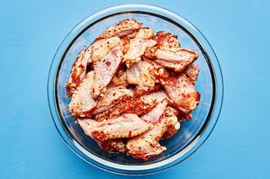 raw chicken wings covered in homemade lemon pepper spice rub in a glass mixing bowl
