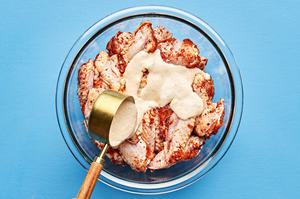 homemade lemon pepper sauce being poured onto raw chicken wings that have been coated in lemon pepper spice rub