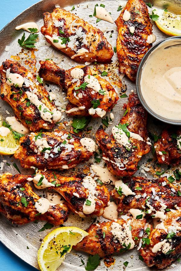 Grilled Lemon Pepper Chicken Wings on a platter drizzled with Lemon Pepper Sauce with a bowl of extra sauce for dipping