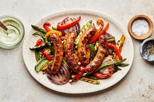 Grilled Sausage and Vegetables on a platter next to bowls of Creamy Dill Dip, salt and pepper
