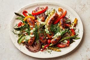 Grilled sausages and vegetables dried with creamy dill dip and sprinkled with fresh dill on a serving platter