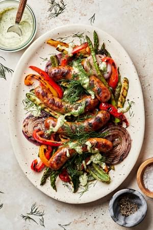 Grilled sausages and vegetables dried with creamy dill dip and sprinkled with fresh dill on a serving platter