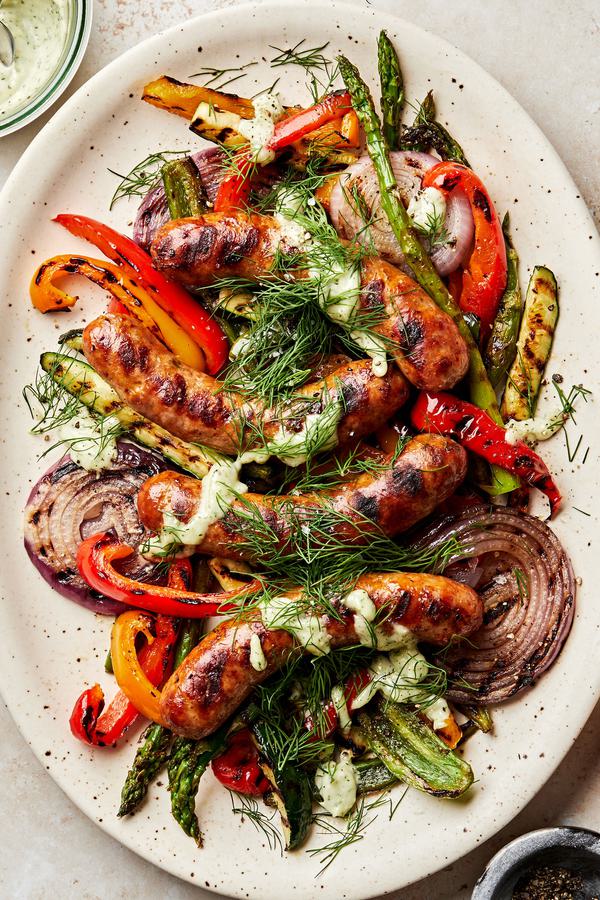 Grilled sausages and vegetables dried with creamy dill dip and sprinkled with fresh dill on a serving platter