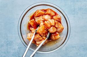 cut up chicken being tossed with tongs in homemade Hawaiian chicken marinade