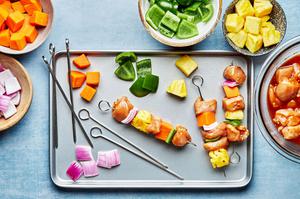 skewers being assembled with sweet potatoes, pineapple, bell pepper, chicken and red onion for Hawaiian chicken kabobs