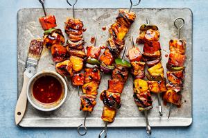 grilled Hawaiian chicken kabobs on a baking sheet brushed with remaining marinade next to a bowl of additional marinade
