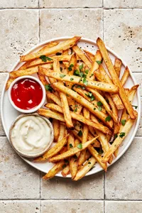 homemade French fries seasoned with salt and pepper, garnished with parsley and served with ketchup and garlic aioli