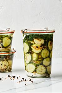 a large jar of homemade dill pickles next to two small jars of homemade pickles stacked on top of each other on the counter