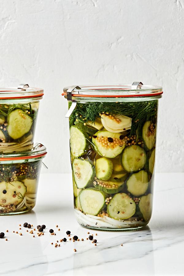 a large jar of homemade dill pickles next to two small jars of homemade pickles stacked on top of each other on the counter