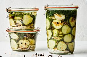 a large jar of homemade dill pickles next to two small jars of homemade pickles stacked on top of each other on the counter